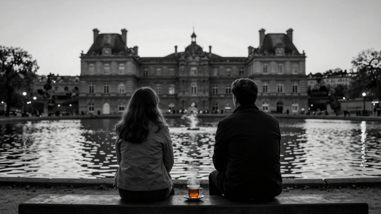 Two people sit silently on a Seine riverside bench at dusk, watching the water as streetlights begin to glow.